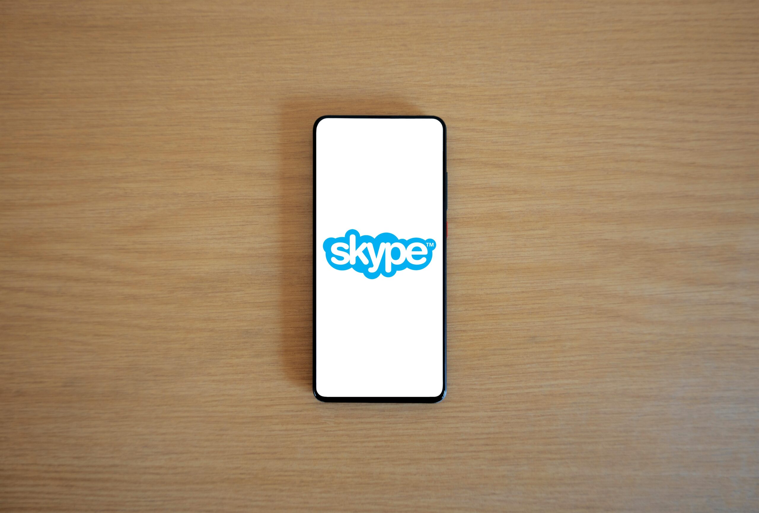 A smartphone top view showcasing Skype logo on screen, placed on a wooden surface.